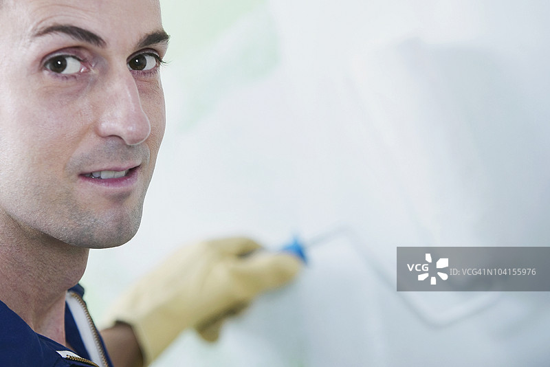 中年男子正在用滚筒刷给墙壁上漆图片素材