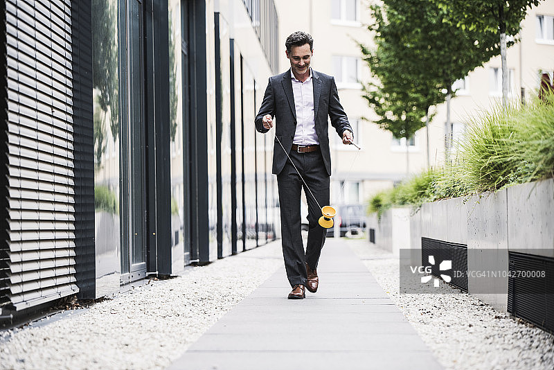 微笑的商务人士在办公楼外玩空竹图片素材