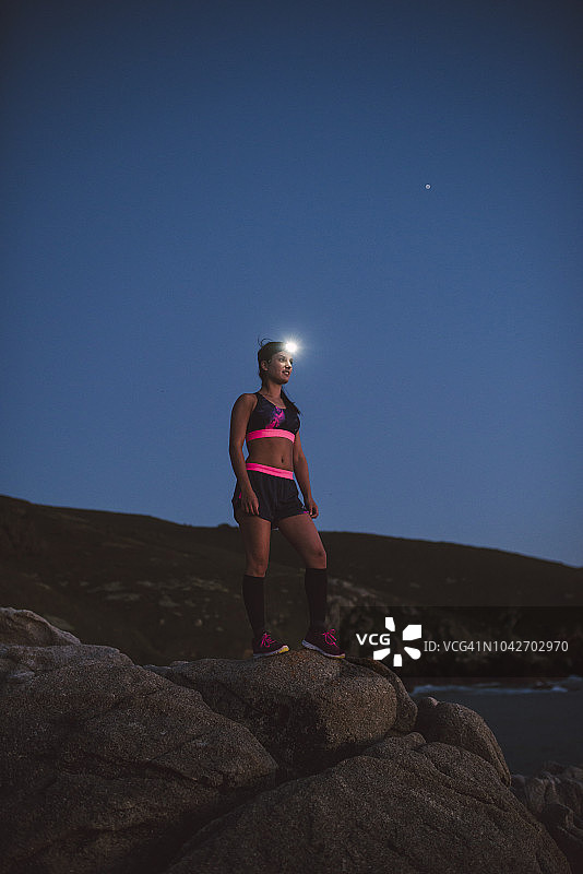 戴着头灯站在傍晚岩石上的运动型女子图片素材