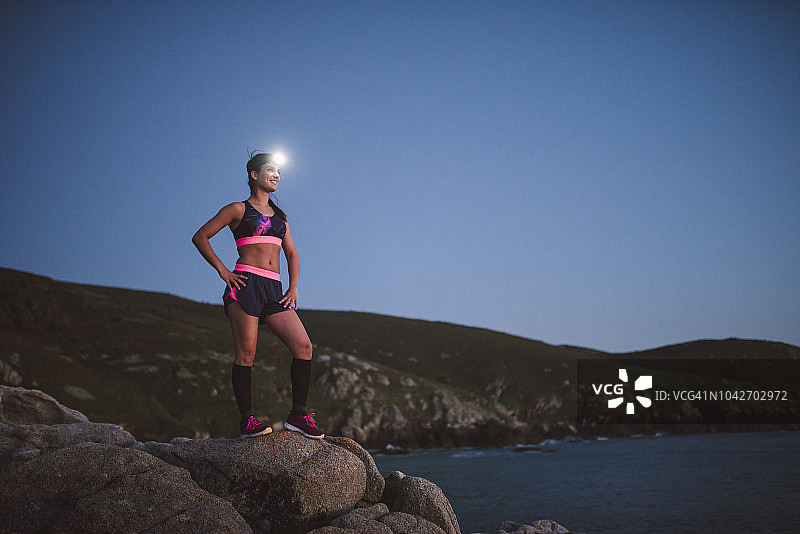 戴着头灯站在傍晚岩石上的运动型女子图片素材