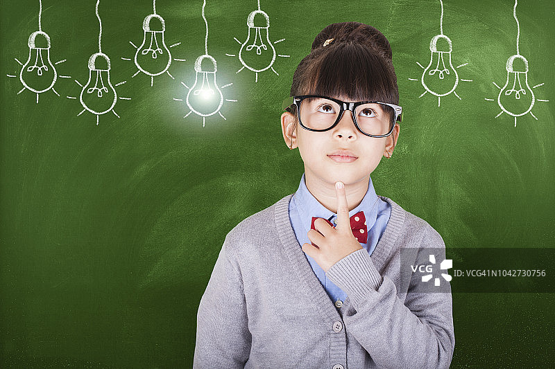 若有所思的亚洲小女孩站在黑板前图片素材