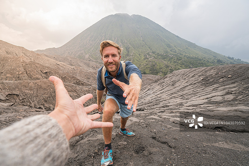 年轻男人在火山徒步，伸手帮助队友图片素材