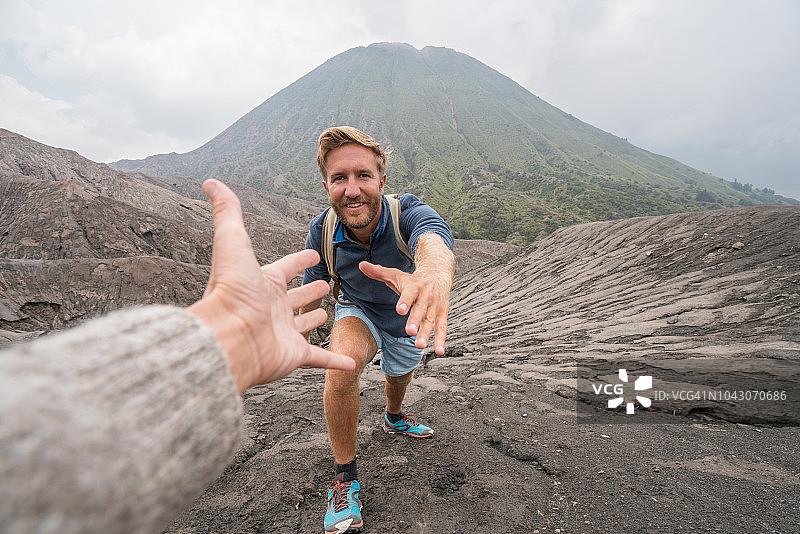 年轻男人在火山徒步，伸手帮助队友图片素材
