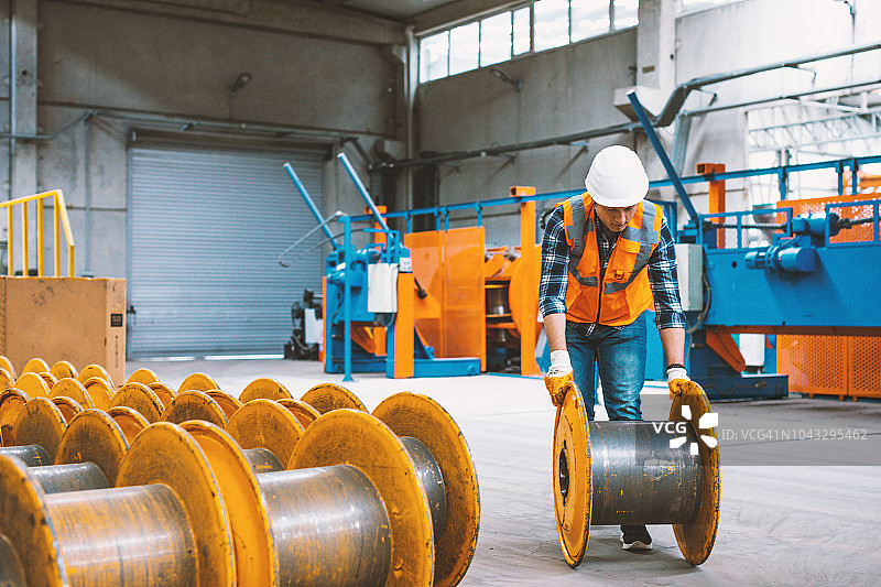 年轻的男工程师在工厂里操作空的钢制电缆卷轴图片素材