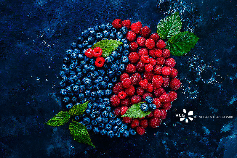 浆果阴阳符号：蓝莓和覆盆子在深色背景上，具有水滴，健康食品平衡概念图片素材