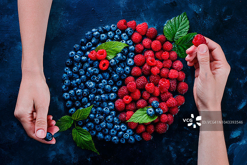 浆果阴阳符号：蓝莓和覆盆子在深色背景上，具有水滴，健康食品平衡概念图片素材