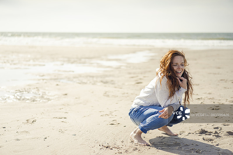 红发女人在海滩上放松，蹲伏着图片素材