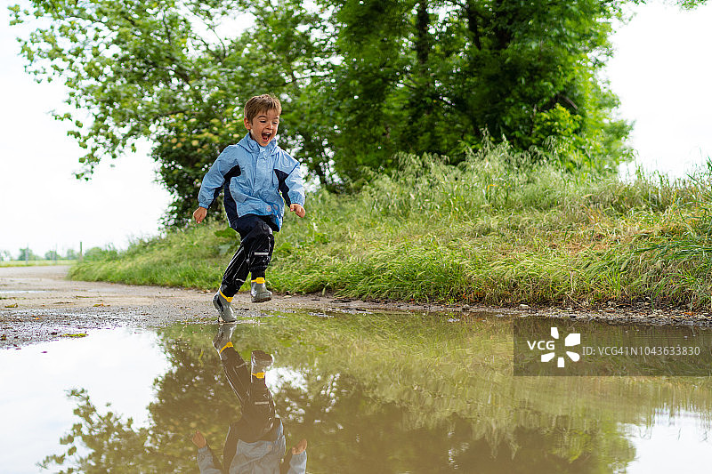 在雨中水坑里奔跑的快乐小男孩图片素材