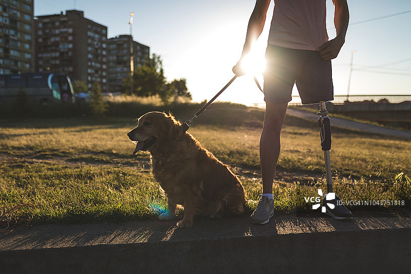 年轻的截肢男子与他的辅助犬站在一起图片素材