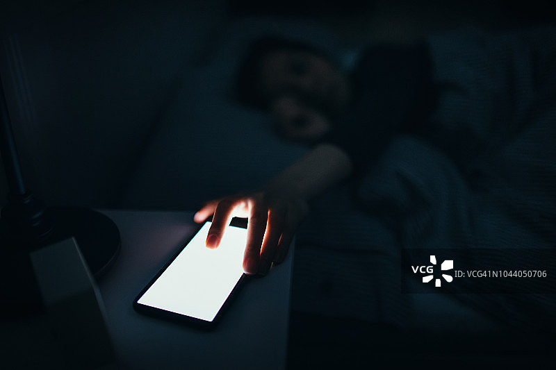 女人在午夜睡觉时伸手关闭智能手机上来自工作的骚扰电话图片素材