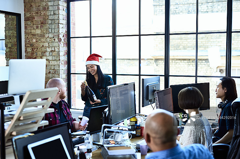 戴着圣诞帽，在现代办公室里拿着香槟的亚洲女人图片素材