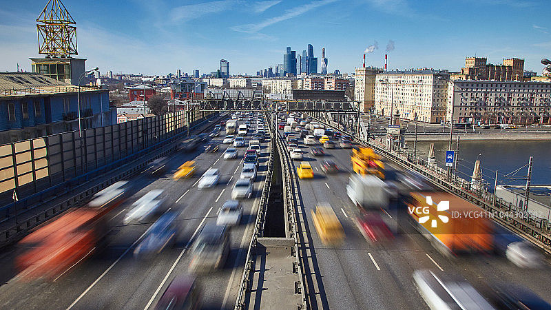 阳光明媚的城市交通俯视图：前景中汽车的模糊运动，背景中办公楼摩天大楼图片素材
