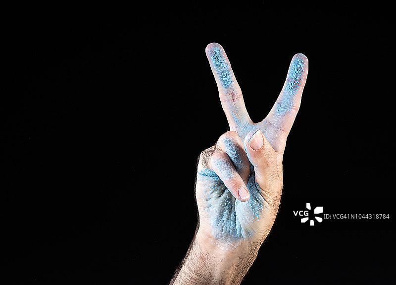 举起手的男人，展示胜利手势，手掌涂有浅蓝色，黑色背景图片素材