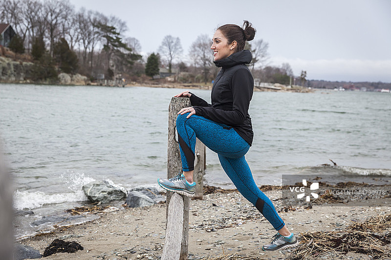 在美国马萨诸塞州欣厄姆海滩上伸展身体的女跑步者侧面照片图片素材