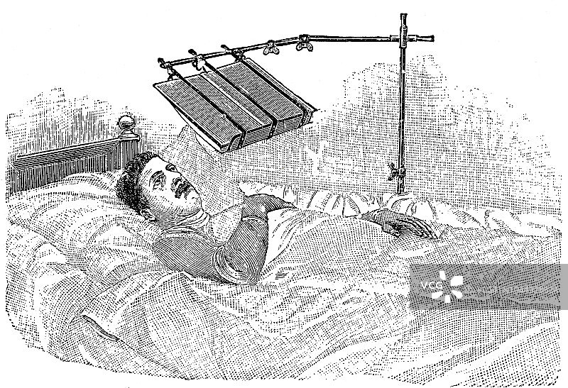 男人躺在床上用特殊免提设备读书图片素材