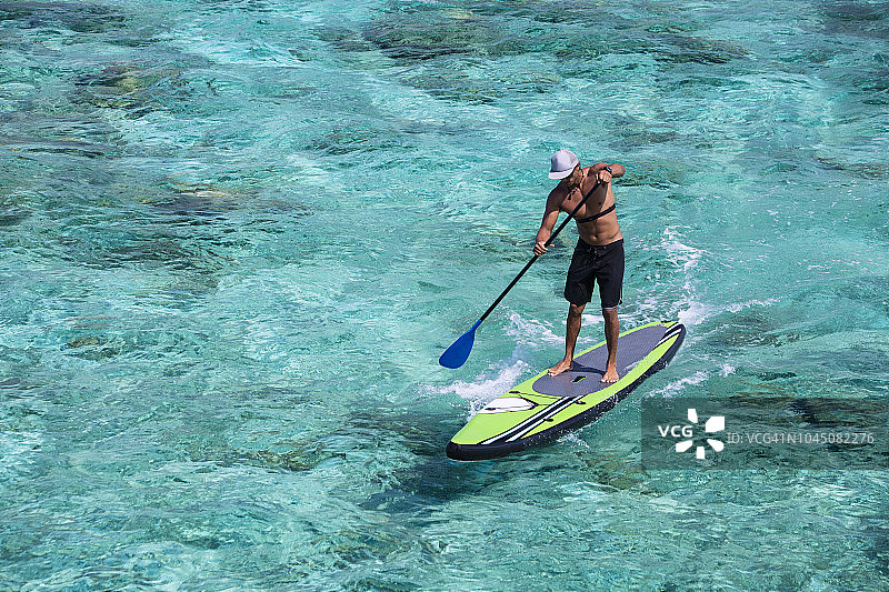 男子站在桨板上，在珊瑚礁泻湖上划桨图片素材