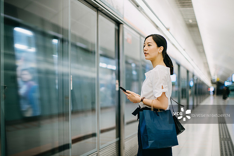 年轻女人提着购物袋在地铁站台上使用智能手机图片素材