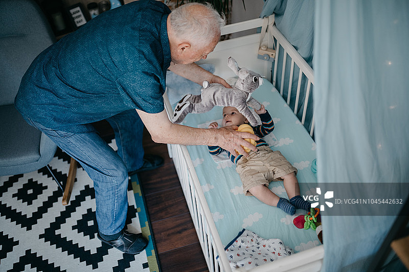 爷爷和躺在婴儿床上的孙子玩耍图片素材