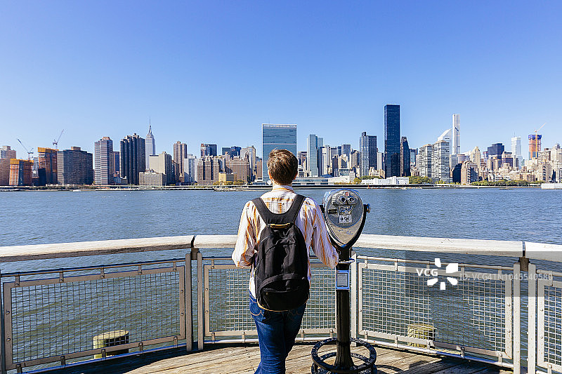 游客背着背包站在投币式双筒望远镜旁，眺望纽约市天际线图片素材
