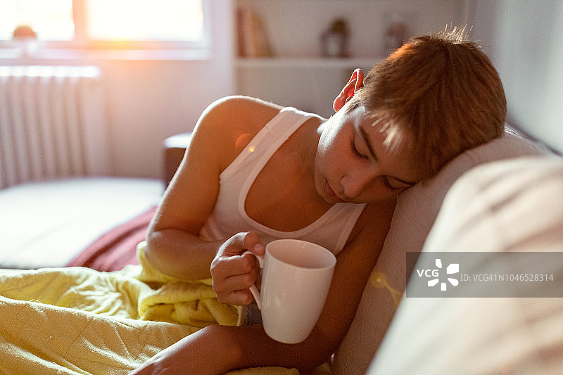 生病的男孩在床上喝茶图片素材