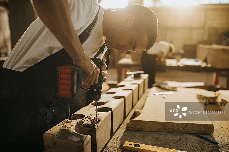 在车间用钻头在木头上工作的男性体力劳动者图片素材