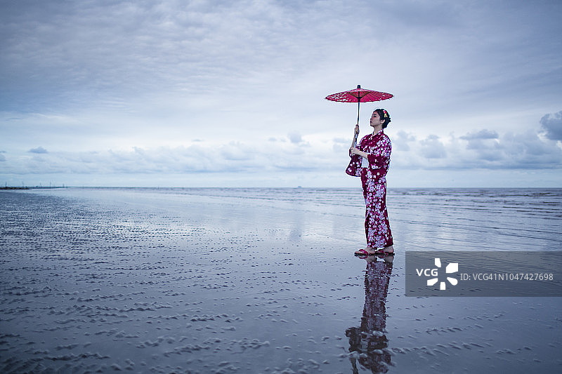 年轻亚洲女子身穿和服在海滩上撑红伞图片素材