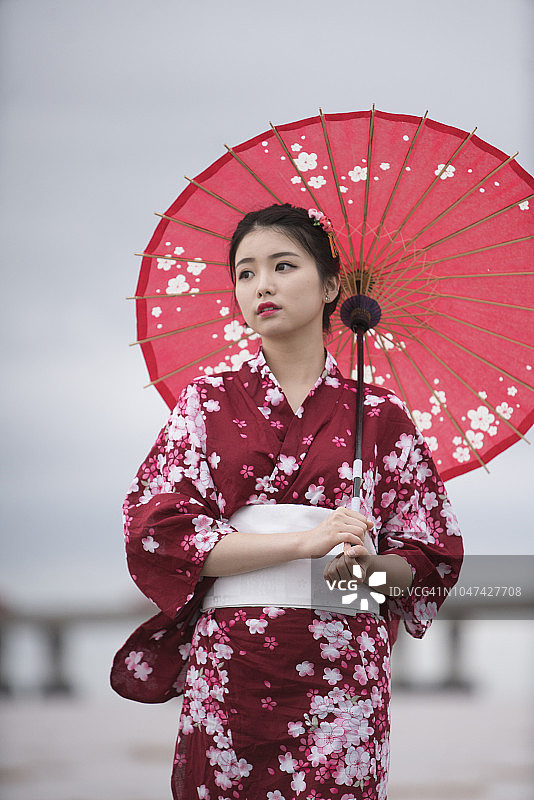 年轻亚洲女子身穿和服在海滩上撑红伞图片素材