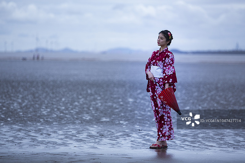 年轻亚洲女子身穿和服在海滩上撑红伞图片素材
