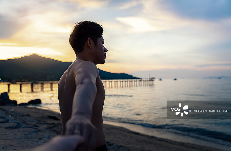 日落时分在海岛沙滩上手牵手散步的幸福情侣图片素材