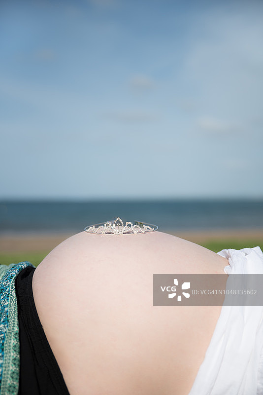 在海滩上的孕妇肚子，肚子上戴着公主皇冠图片素材