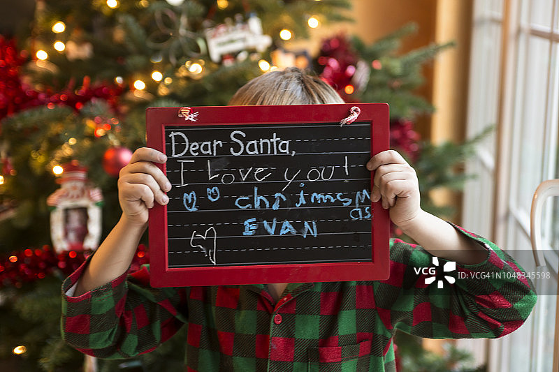 男孩拿着写给圣诞老人的留言黑板图片素材