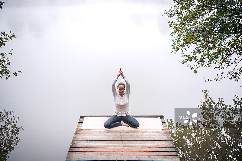 薄雾清晨，女性在湖边练习瑜伽图片素材