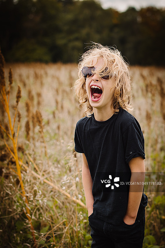 在田野里戴着墨镜大笑的长发金发男孩图片素材