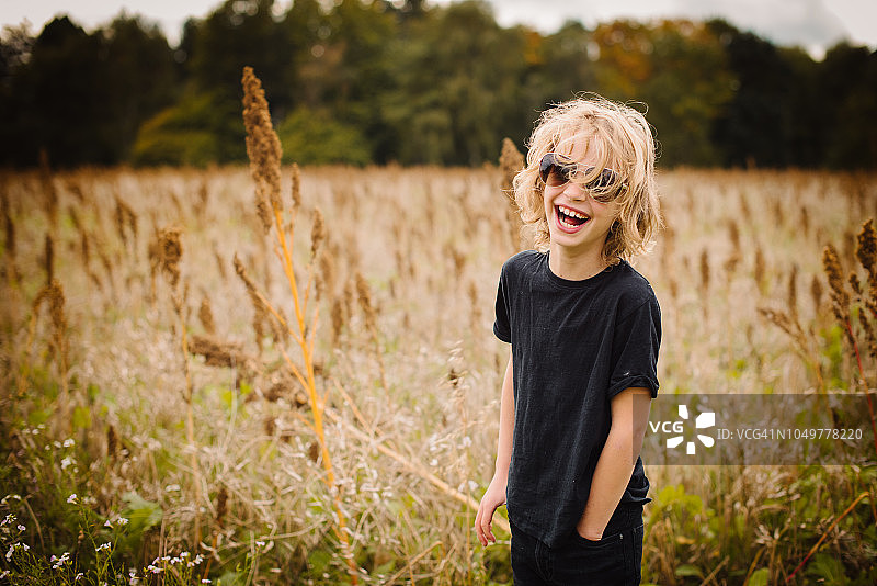 在田野里戴着墨镜大笑的长发金发男孩图片素材