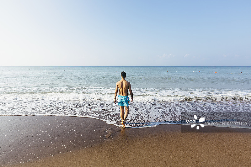 在沙滩上走向大海的泳装男子背影图片素材
