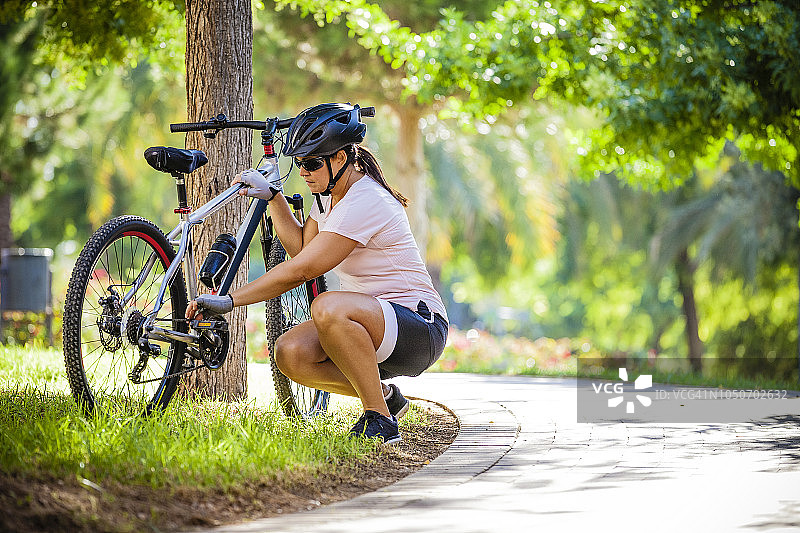 中年妇女在户外自行车旁蹲着修理链条图片素材