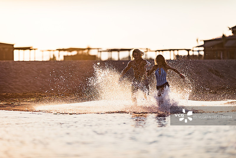 日落时在海边追逐嬉戏的年轻情侣图片素材