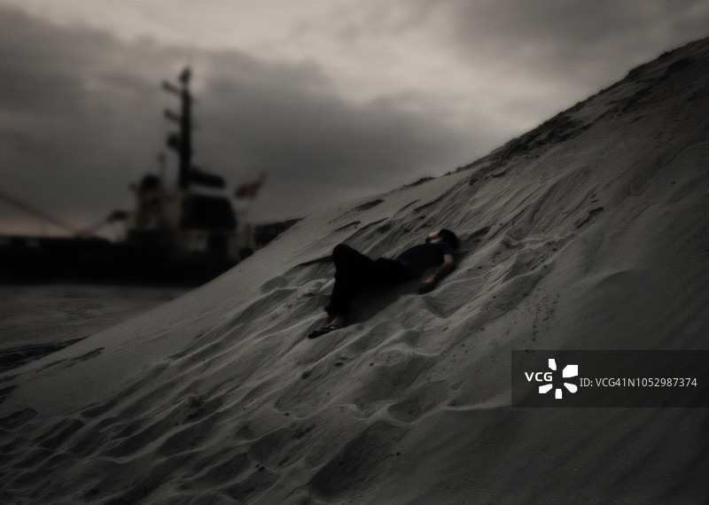 被遗弃的男人躺在沙丘上，船只驶近图片素材