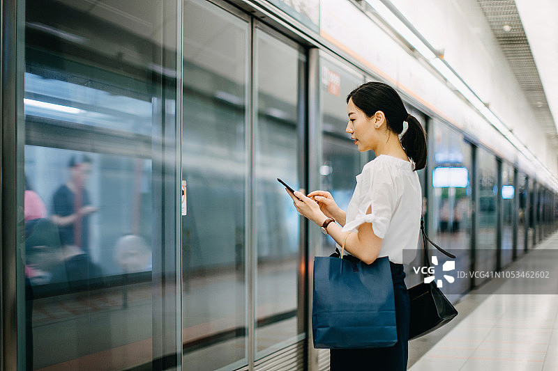 年轻女人提着购物袋在地铁站台上使用智能手机图片素材