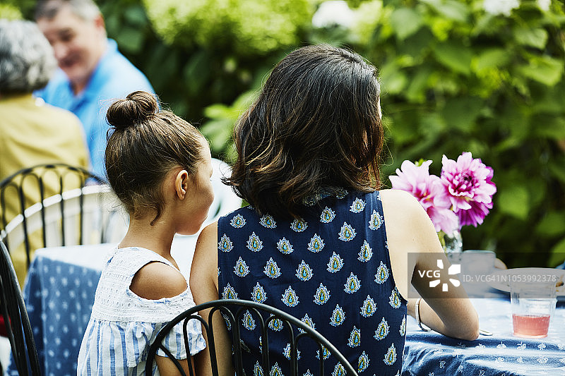 母亲和女儿在花园派对上一起坐在桌旁的背影图片素材