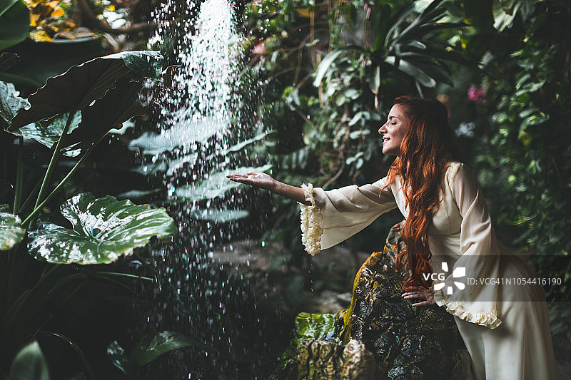 身穿白色连衣裙的女人站在瀑布前图片素材