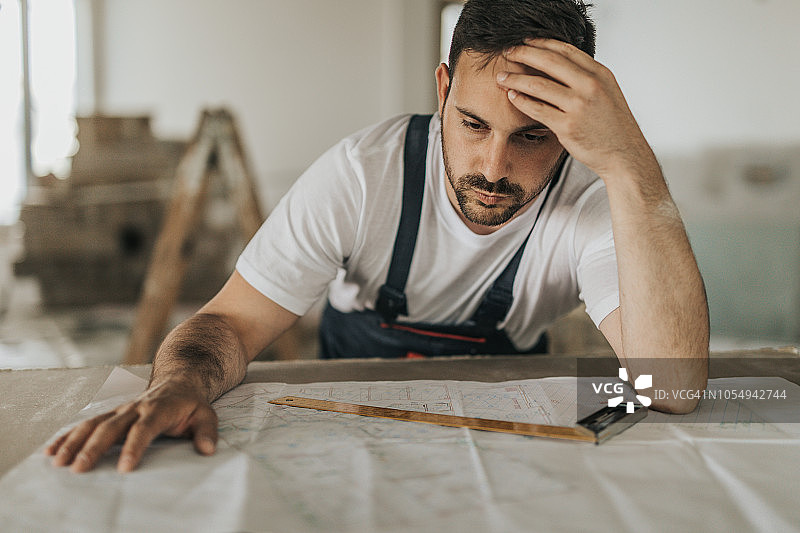 沮丧的手工工人在建筑工地使用蓝图时遇到问题。图片素材