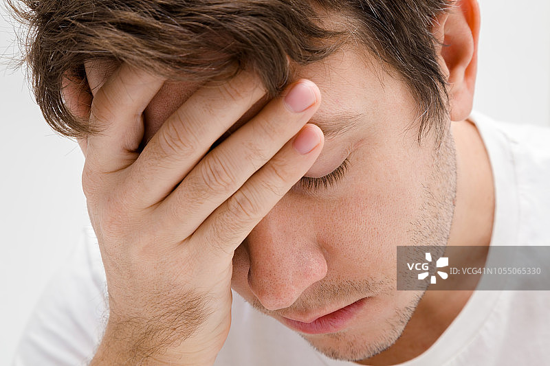 年轻孤独、悲伤的男人摸着头。遭受心碎、倦怠或其他心理问题的折磨。记忆障碍。男性问题。面部特写。成年棕发男子。图片素材