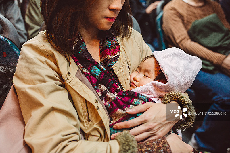 年轻漂亮的妈妈在公交车上用婴儿背带抱着熟睡的可爱宝宝图片素材