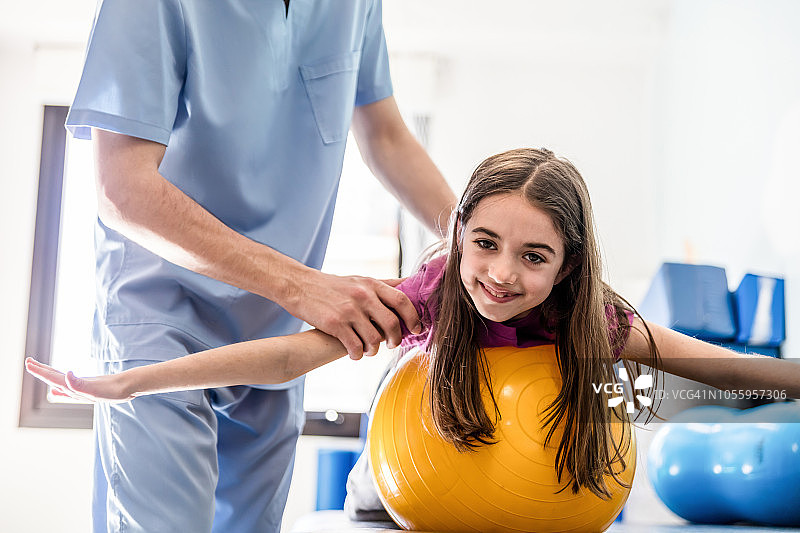 在职业治疗中靠在球上看着镜头的可爱小女孩图片素材