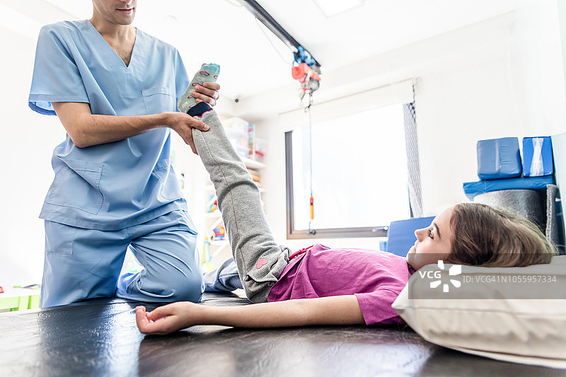 身份不明的理疗师帮助一个小女孩伸展腿，而她正躺在手术台上图片素材
