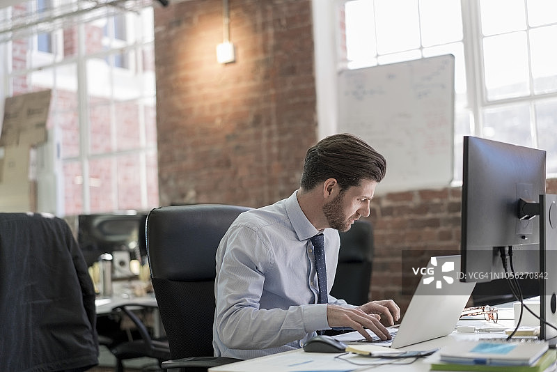 自信的男士在办公桌前使用笔记本电脑图片素材