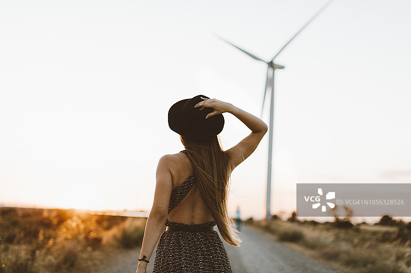 傍晚乡间小路上，背景是风车的年轻女子背影图片素材