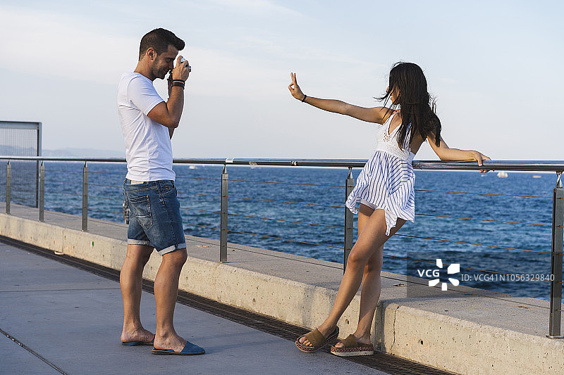 年轻的都市情侣在海边拍照，女士做出和平手势图片素材