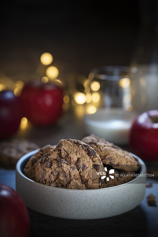 深色木质背景上的巧克力曲奇、一杯牛奶和苹果图片素材